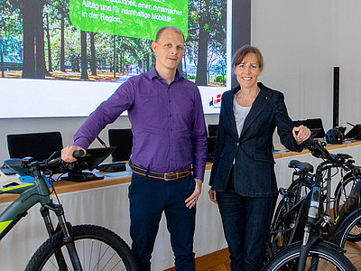 Auf diesem Bild sind zwei Personen mit Fahrrädern in einem Saal zu sehen.